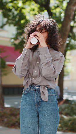 Happy-young-woman-enjoying-drinking-morning-coffee-hot-drink-relaxing-taking-a-break-on-city-street