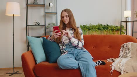 Cheerful-young-woman-sitting-on-sofa,-using-mobile-phone-share-messages-on-social-media-application