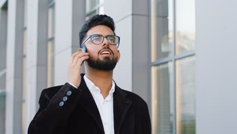 Empresario-Indio-Teniendo-Una-Conversación-Remota-Hablando-Por-Teléfono-Inteligente,-Chismes-De-Buenas-Noticias-En-Las-Calles-De-La-Ciudad