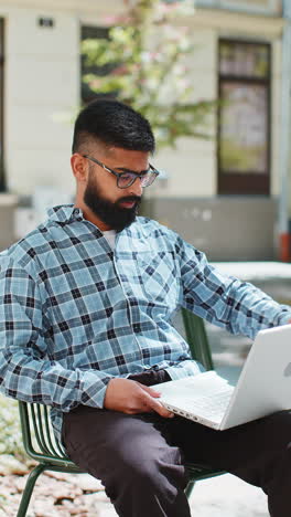 Indischer-Freiberufler,-Der-Online-Arbeitet-Und-Mit-Dem-Laptop-Auf-Der-Straße-In-Der-Stadt-Auf-Der-Website-Surft