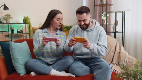 Happy-family-married-couple-man-woman-playing-shooter-video-app-games-online-on-smartphone-at-home