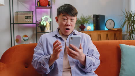 Happy-asian-man-at-home-use-smartphone-typing-browsing-wow-yes-found-out-great-big-win-celebrate