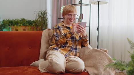 Young-woman-sitting-on-sofa-at-home,-using-smartphone-share-messages-on-social-media-application