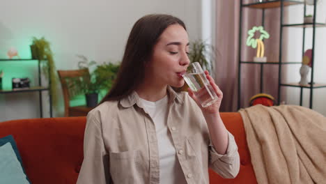 Una-Joven-Sedienta-Sentada-En-Casa-Sosteniendo-Un-Vaso-De-Agua-Natural-Haciendo-Sorbos-Bebiendo-Agua-Sin-Gas