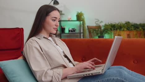 Young-woman-freelancer-sitting-on-couch-closing-laptop-pc-after-finishing-work-in-room-at-home