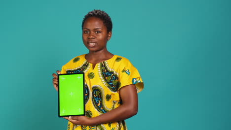 Happy-natural-girl-showing-a-green-screen-against-blue-background