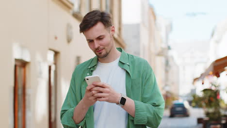 Hombre-Feliz-Usando-Un-Teléfono-Inteligente-Escribiendo-Mensajes-De-Texto-De-Aplicaciones-De-Redes-Sociales-Mensajes-De-Correo-Electrónico-En-Las-Calles-De-La-Ciudad