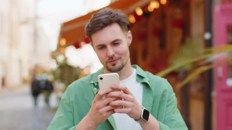 Man-using-smartphone-typing-text-messages-browsing-internet,-finishing-work,-looking-at-camera