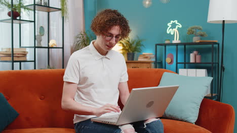 Happy-Caucasian-man-sitting-on-couch-closing-laptop-and-relaxing-after-finishing-work-in-living-room