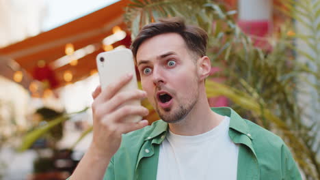 Excited-happy-winner-man-using-smartphone-looking-amazed-at-screen-celebrating-win-good-message-news