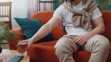 Thirsty-Caucasian-man-sitting-at-home-holding-glass-of-natural-aqua-make-sips-drinking-still-water