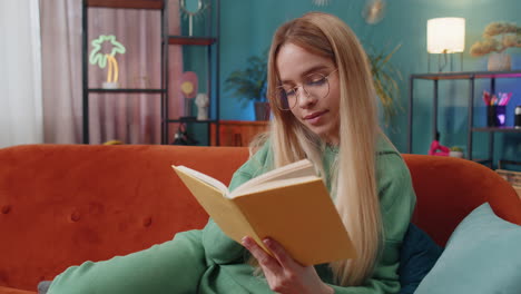 Young-woman-relaxing-interesting-book-turning-pages-smiling-enjoying-literature-taking-rest-on-sofa