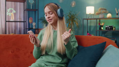 Happy-caucasian-woman-in-wireless-headphones-relaxing-sits-on-sofa-at-home-listening-favorite-music