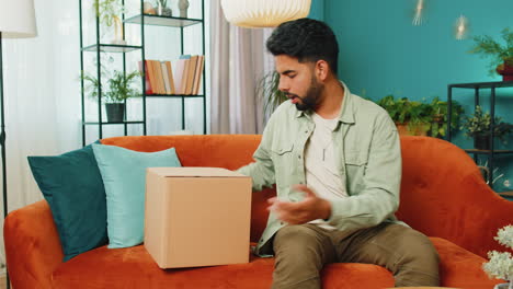 Happy-Arabian-man-shopper-unpacking-cardboard-box-delivery-parcel-online-shopping-purchase-at-home