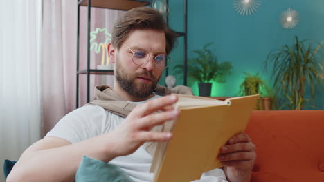 Young-man-relaxing-interesting-book-turning-pages-smiling-enjoying-literature-taking-a-rest-on-sofa