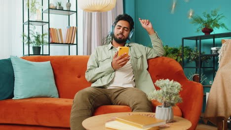 Hombre-Feliz-Y-Relajado-Con-Auriculares-Inalámbricos-Bailando-Escuchando-Música-Rock-N-Roll-Favorita-En-El-Sofá-De-Casa