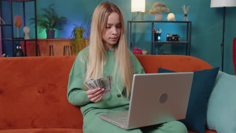 Smiling-young-woman-counting-money-cash-and-use-laptop-pc-calculate-domestic-income-earnings-at-home