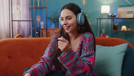 Happy-young-woman-in-wireless-headphones-relaxing-sitting-on-sofa-at-home-listening-favorite-music