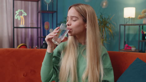 Thirsty-Caucasian-woman-sitting-at-home-holding-glass-of-natural-aqua-make-sips-drinking-still-water