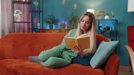 Young-woman-relaxing-interesting-book-turning-pages-smiling-enjoying-literature-taking-rest-on-sofa