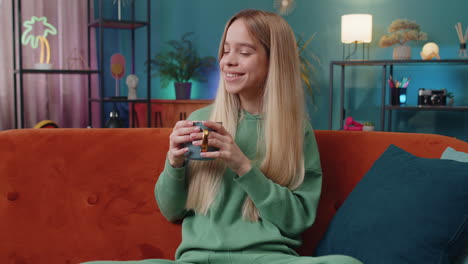 Attractive-smiling-woman-girl-drinking-a-cup-of-coffee-or-herbal-tea-at-home-couch-in-the-morning