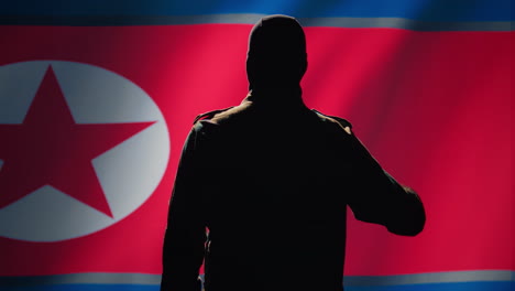 Soldado-Haciendo-Un-Gesto-De-Saludo-Con-La-Mano-Hacia-La-Bandera-De-Corea-Del-Norte
