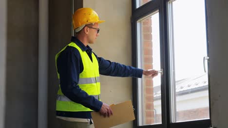 Männlicher-Baumeister-Mit-Klemmbrett,-Das-Fenster-überprüft.-Baugeschäft-Und-Gebäudekonzept-Männlicher-Baumeister-Mit-Klemmbrett,-Das-Fenster-überprüft