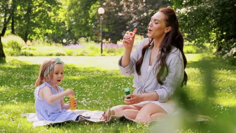 Mutter-Mit-Tochter-Bläst-Seifenblasen-Im-Park.Familie,-Mutterschaft-Und-Menschen-Konzept-Glückliche-Mutter-Mit-Kleiner-Tochter-Bläst-Seifenblasen-Im-Sommerpark-Oder-Garten