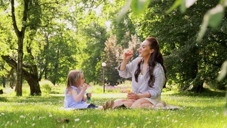 Madre-Con-Hija-Soplando-Pompas-De-Jabón-En-El-Parque.concepto-De-Familia,-Maternidad-Y-Personas-Madre-Feliz-Con-Hija-Pequeña-Soplando-Pompas-De-Jabón-En-El-Parque-O-Jardín-De-Verano