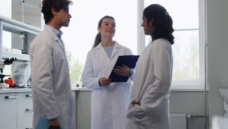 International-Group-of-Scientists-in-Laboratory.science-research,-work-and-people-concept-international-group-of-happy-scientists-with-clipboards-discussing-report-in-laboratory