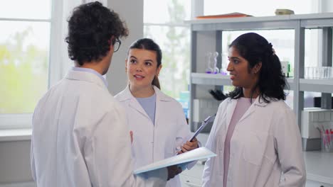 International-Group-of-Scientists-in-Laboratory.science-research,-work-and-people-concept-international-group-of-happy-scientists-with-clipboards-discussing-report-in-laboratory