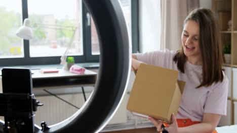 Happy-Girl-Blogger-Unpacking-Parcel-Box-at-Home.blogging,-technology-and-people-concept-happy-smiling-girl-or-beauty-blogger-with-ring-light-and-smartphone-unpacking-parcel-box-with-cosmetics-at-home