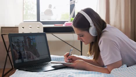 Estudiante-Con-Computadora-Portátil-Aprendiendo-En-Línea-En-Casa.-Escuela,-Educación-En-Línea-Y-Concepto-De-Aprendizaje-Electrónico-Adolescente-Estudiante-Con-Computadora-Portátil-Teniendo-Clase-De-Química-Y-Escribiendo-En-Un-Cuaderno-Acostado-En-La-Cama-En-Casa