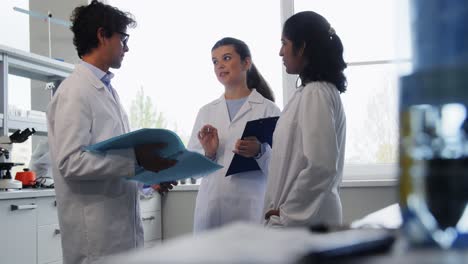 International-Group-of-Scientists-in-Laboratory.science-research,-work-and-people-concept-international-group-of-happy-scientists-with-clipboards-discussing-report-in-laboratory