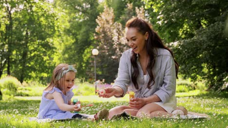 Madre-Con-Hija-Soplando-Pompas-De-Jabón-En-El-Parque.concepto-De-Familia,-Maternidad-Y-Personas-Madre-Feliz-Con-Hija-Pequeña-Soplando-Pompas-De-Jabón-En-El-Parque-O-Jardín-De-Verano