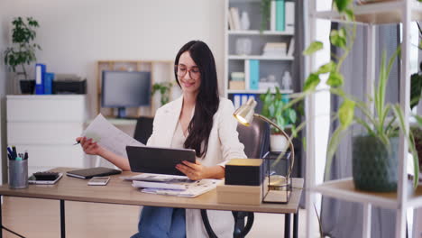 Satisfied-Businesswoman-Using-Tablet-and-Analyzing-Documents