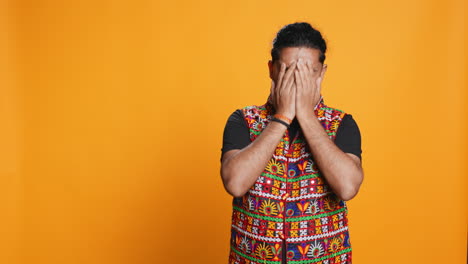 Anxious-man-covering-face-with-palms,-feeling-worried,-studio-background