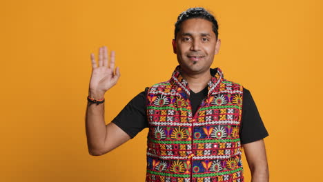 Portrait-of-jolly-man-smiling-and-waving-hand,-saluting,-studio-background