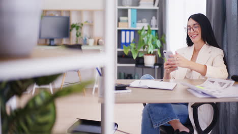 Glückliche-Frau-Im-Büro-Verwaltet-Ihr-Geschäft-Mit-Dem-Smartphone