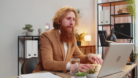 Business-man-sitting-at-workplace-desk-drinking-water-while-working-with-laptop-in-home-office