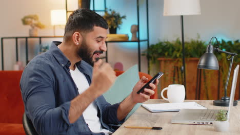 Happy-amazed-Indian-man-guy-working-on-smartphone-celebrate-victory-winning-lottery-at-home-office