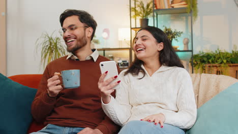 Happy-girlfriend-boyfriend-couple-browse-social-media-applications-together-on-smartphone-at-home