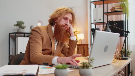 Bored-sleepy-tired-businessman-worker-working-on-laptop-computer-leaning-on-hand-at-home-office-desk