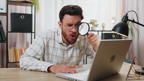 Surprised-businessman-working-on-laptop-holding-magnifying-glass-wow-expression-searching-analyzing