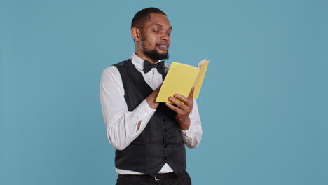 Young-doorman-hotelier-reading-a-book-on-his-work-break-in-studio