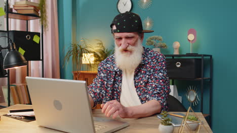 Senior-man-working-on-laptop-computer-at-home-office-showing-thumbs-down-sign-dislike-disapproval