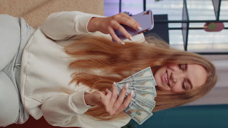 Smiling-happy-young-woman-at-home-counting-money-cash-use-smartphone,-income,-saves,-lottery-win