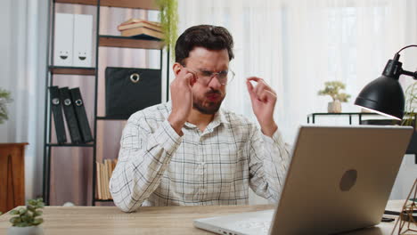 Overworked-young-Indian-bearded-businessman-suffering-from-eye-strain-and-headache-working-on-laptop