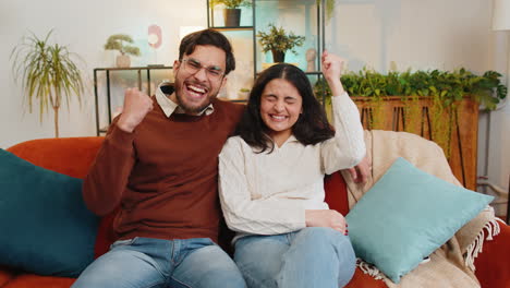 Indian-couple-celebrating-success-clenching-fists-showing-thumbs-up-and-giving-high-five-at-home