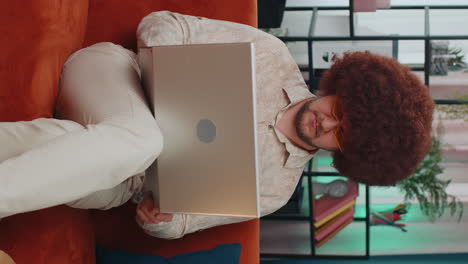 Young-man-freelancer-sitting-on-sofa-closing-laptop-pc-after-finishing-work-in-living-room-at-home